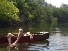 a man laying on top of a boat in the middle of a lake next to trees