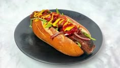 a hot dog with mustard, ketchup and relish on a black plate