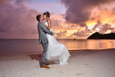 a bride and groom standing on the beach at sunset with clouds in the sky behind them