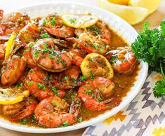 a white bowl filled with cooked shrimp and garnished with parsley next to lemon wedges