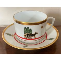 a cup and saucer with an animal motif on the side, sitting on a wooden table