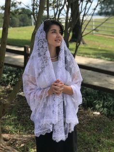 a woman wearing a white veil and black pants standing next to a tree in a park