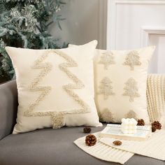 two white pillows sitting on top of a gray couch next to a christmas tree pillow