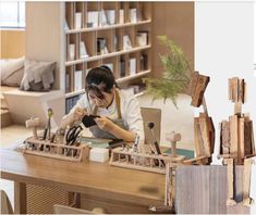 a woman sitting at a wooden table working on some kind of crafting project in front of a bookshelf