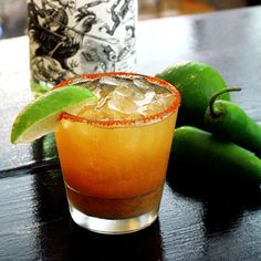 a close up of a drink on a table with green peppers and bottles in the background