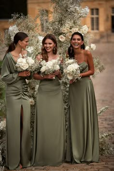 three bridesmaids standing in front of an arch with flowers and greenery on it