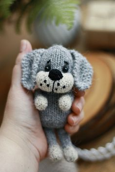 a hand holding a small knitted dog in it's right hand, with a plant behind it