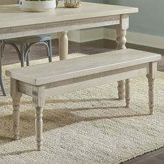 a white table and bench with vases on top of it next to a rug