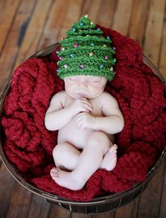 a newborn baby wearing a crocheted christmas tree hat on top of a red blanket