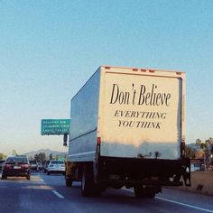 a white truck driving down a street next to a traffic light with a sign that says don't believe everything you think