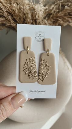 a pair of earrings is shown in front of a white vase with dried flowers on it