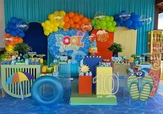 a birthday party with balloons and decorations on the table in front of a blue backdrop