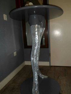 a mannequin's legs are covered in silver sequins and stand on a round table