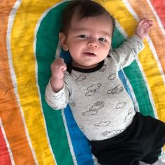 a baby laying on top of a rainbow blanket with his hands up in the air