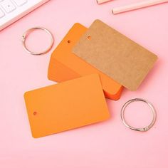 three orange tags sitting on top of a pink table next to a keyboard and pencils