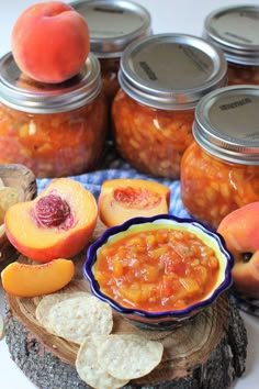 some peaches and other fruit are in jars on a tree stump with crackers