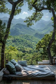 a bed sitting on top of a wooden deck next to a lush green forest covered hillside