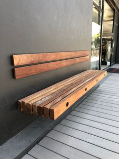 a wooden bench sitting on the side of a building next to a wall with windows