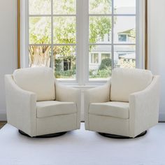 two white chairs facing each other in front of a window with trees outside the window