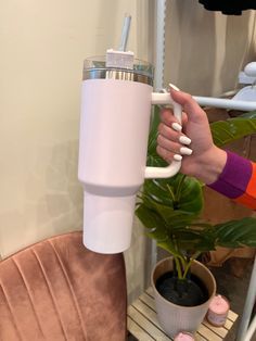 a woman is holding a white cup with a straw in it while sitting on a pink chair