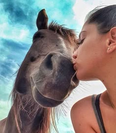 a woman kissing a horse on the nose in front of a blue sky with clouds