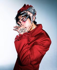 a man with tattoos on his face and hands in front of his face, wearing a red shirt