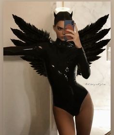 a woman in a black bodysuit taking a selfie with her cell phone while wearing angel wings