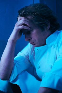 a man sitting in a chair with his hands on his head while looking at something