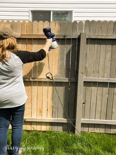 a woman is using a power drill to paint the fence outside her house and yard