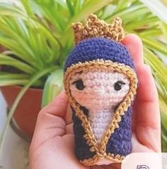 a small crocheted doll with a crown on it's head is held in front of a potted plant