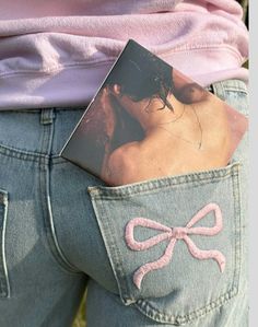 the back of a woman's jeans with a pink bow on it and a book in her pocket