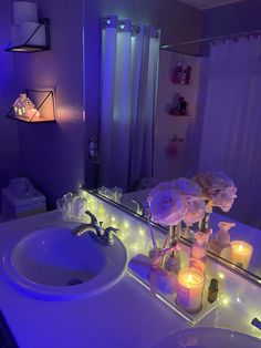 a lighted bathroom vanity with flowers and candles on the counter top, next to a mirror