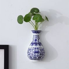 a blue and white vase with a plant in it on a wall next to a framed photograph