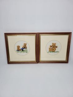 two framed teddy bears sitting next to each other on a white wall with brown trim