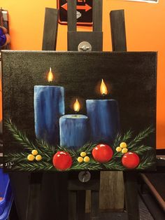 a painting of three blue candles on a black board with holly and berries around it