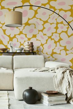 a white couch sitting under a lamp next to a wall with pink and yellow flowers on it