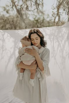 a woman holding a baby in her arms while standing next to a white tarp