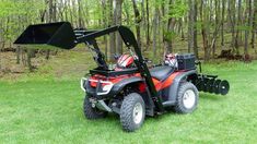 a red and black atv with a snow plow attached to the front wheel on grass