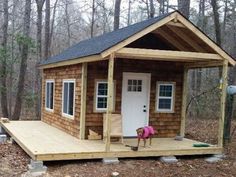 a small wooden cabin in the woods with a dog standing on the porch and door