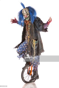 a creepy clown riding a unicycle with blue hair and makeup stock photo