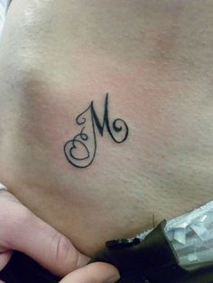 a woman's lower back tattoo with the letter m in cursive font