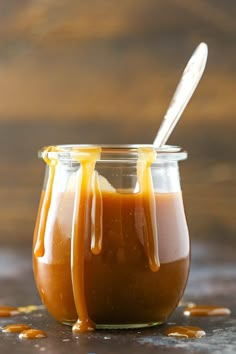 two jars filled with caramel sauce on top of a wooden table next to a spoon