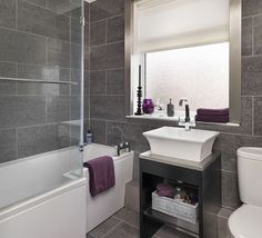 a bathroom with gray tiles and white fixtures, including a sink, toilet, tub, shower stall and bathtub