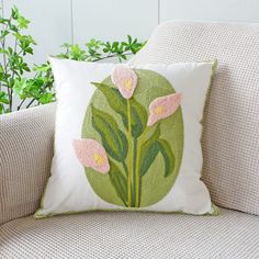 a pillow with pink flowers on it sitting on a couch next to a potted plant