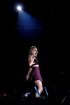 a woman standing on top of a stage with a microphone in her hand and lights behind her