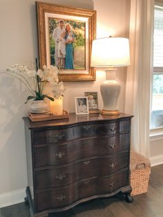 an old dresser with flowers and pictures on it in front of a framed portrait above it