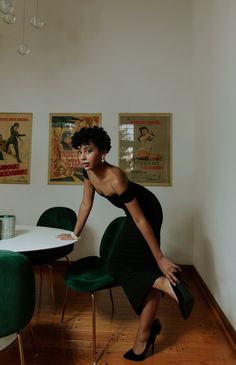 a woman in a black dress leaning on a green chair