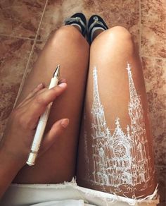 a woman is drawing on her leg with white paint and a pen while sitting on the floor