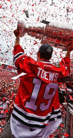 a hockey player holding up the stanley cup in front of a crowd of fans and confetti