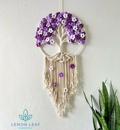 a white wall hanging with purple and white flowers on it next to a potted plant